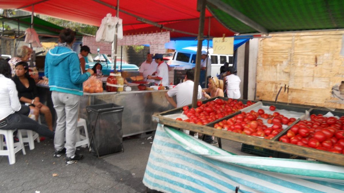 Barraca de tomates em feira livre, com feirantes e clientes