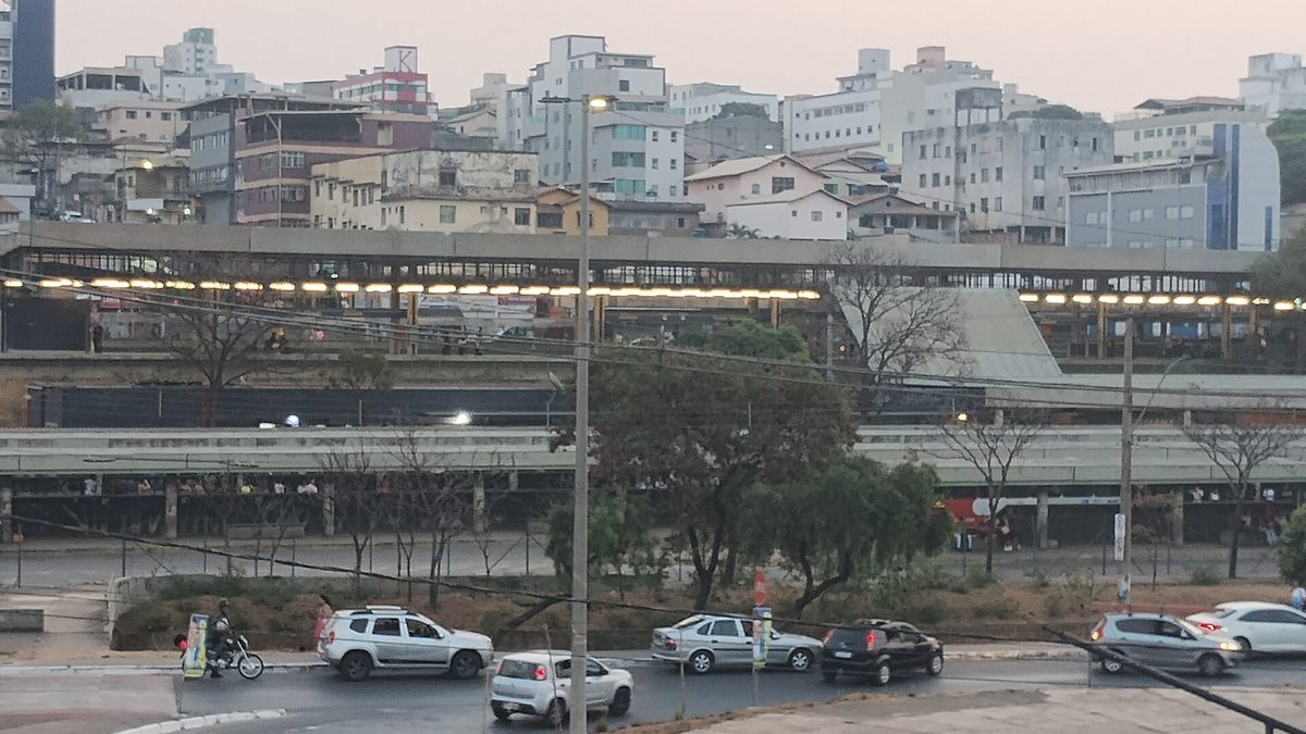 Estação Eldorado do metrô ao entardecer, com carros na rua em frente e prédios de Contagem ao fundo
