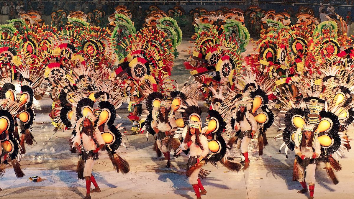 Dançarinos com fantasias de penas coloridas se apresentam na arena do Bumbódromo, em Parintins