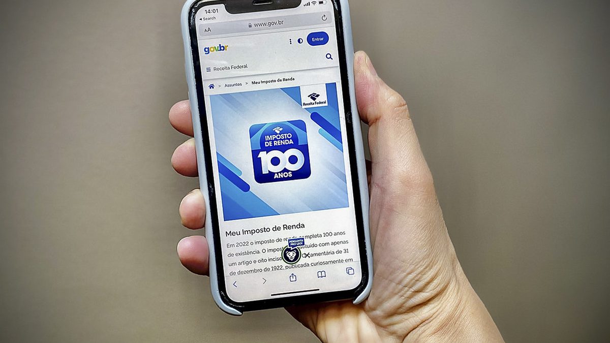 Mão segura celular com a página Meu Imposto de Renda, da Receita Federal, aberta na tela