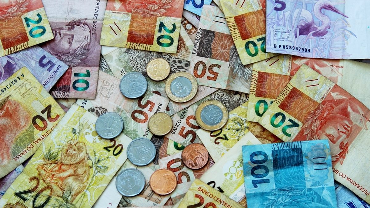 Cédulas e moedas de real de vários valores espalhadas sobre uma mesa