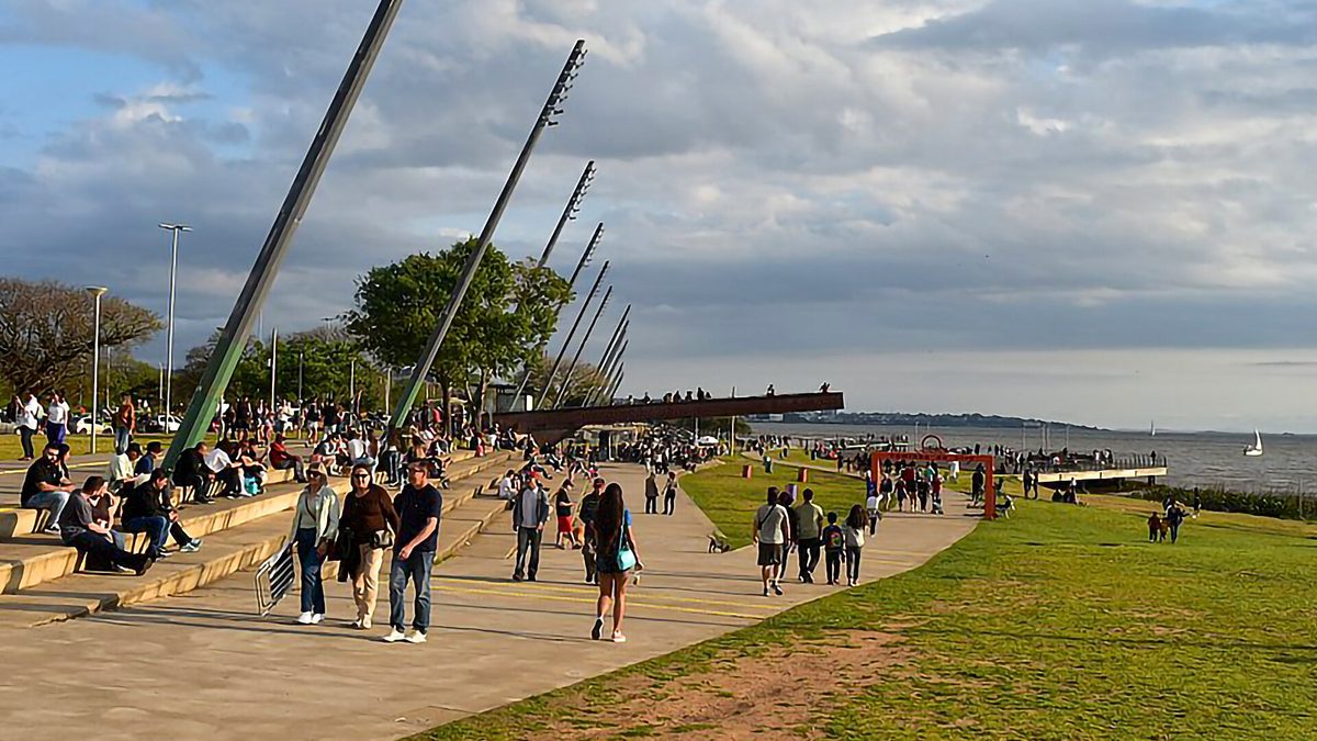 Pessoas caminham na orla do Guaíba, em Porto Alegre, sob céu com nuvens