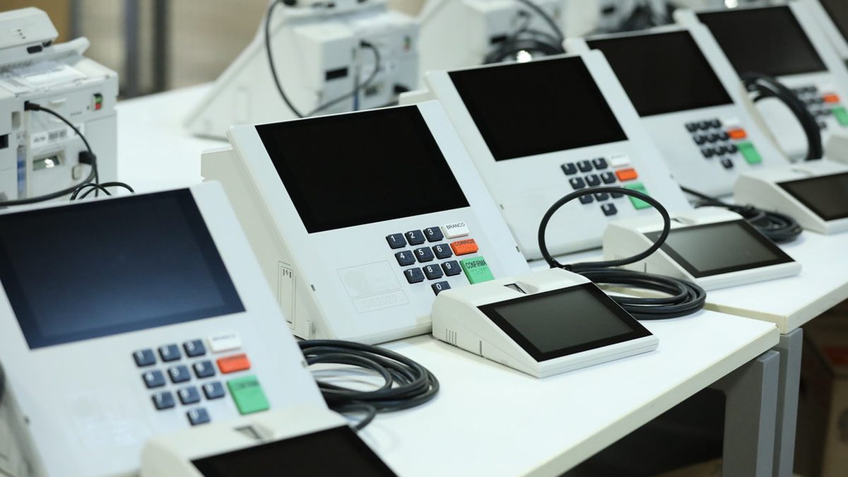 Urnas eletrônicas enfileiradas sobre bancadas, preparadas para a votação