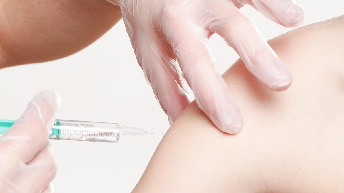 Profissional de saúde com luvas aplica vacina no braço de uma pessoa