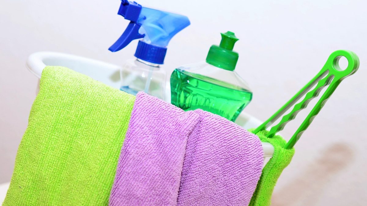 Borrifadores, frasco de detergente e panos de limpeza dentro de um balde